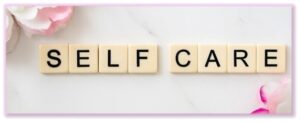 the words Self Care spelled in tiles with pink flowers in background