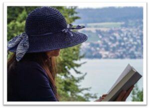 Woman in a blue hat outside by the ocean reading a book